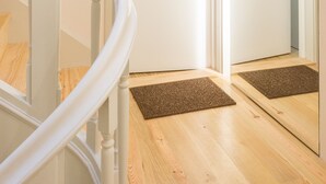 Eine Treppe mit weißen Balustraden führt zu einer Tür, in deren Spiegel sich die Tür selbst spiegelt, und einem Fußabstreifer auf dem Boden.