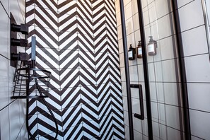 Clean lines and a chevron tile pattern define this contemporary bathroom, featuring a glass shower enclosure and towel rack.