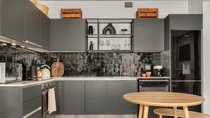 A modern kitchen with grey cabinets, a black backsplash, and a wooden dining table with stools. - The Signature 102 (Cape Town)