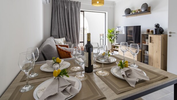 A dining table set with wine glasses, plates, and a bottle, with a sofa and curtains in the background.