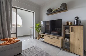 Ein modernes Wohnzimmer mit einem grauen Sofa, einem Flachbildfernseher, Holzschränken und einem großen Fenster mit Aussicht.