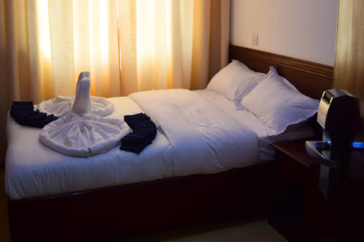 A hotel room with a neatly made bed, a bedside table with a lamp, and a window with curtains.