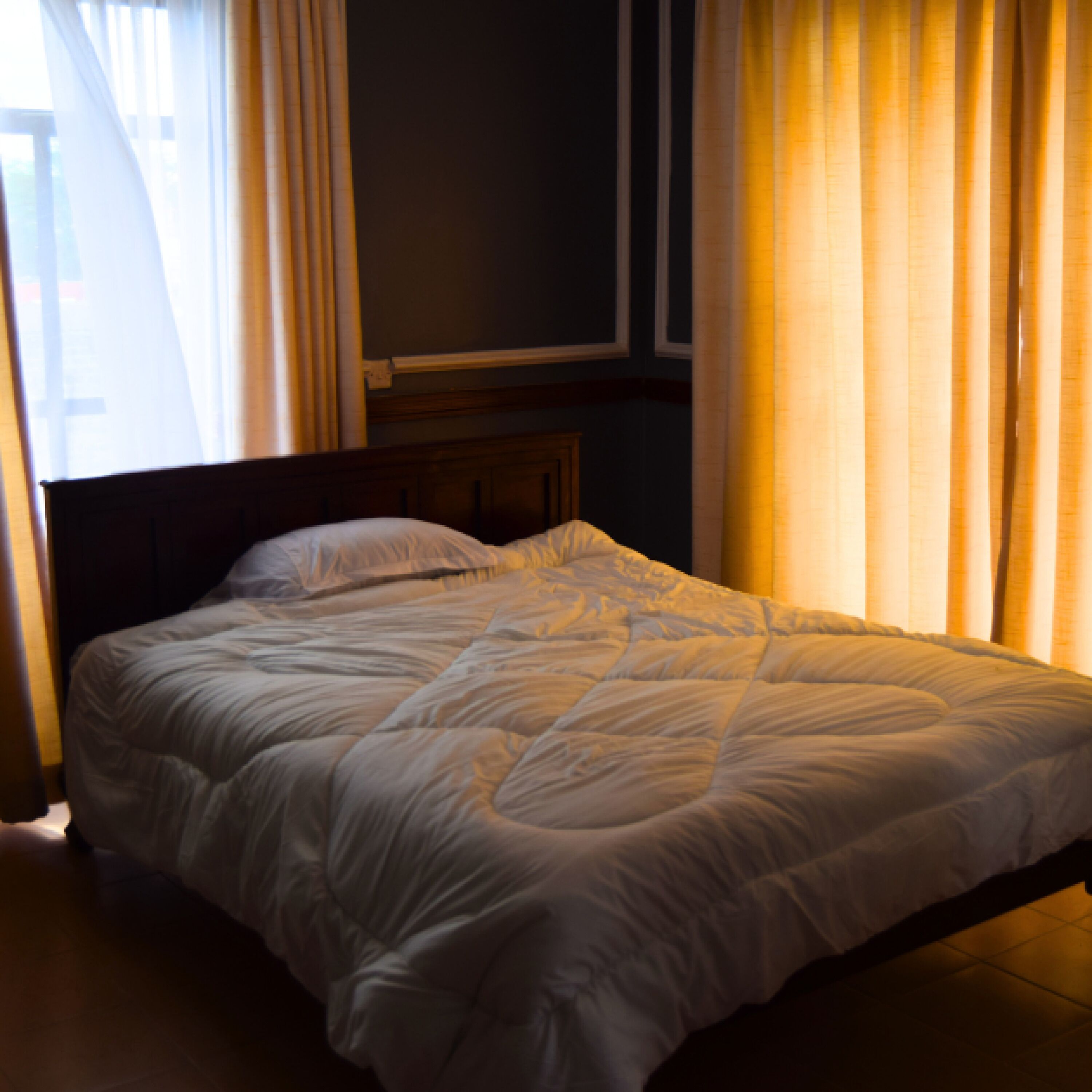 Una cama bien hecha con cabecera de madera en una habitación con poca luz.