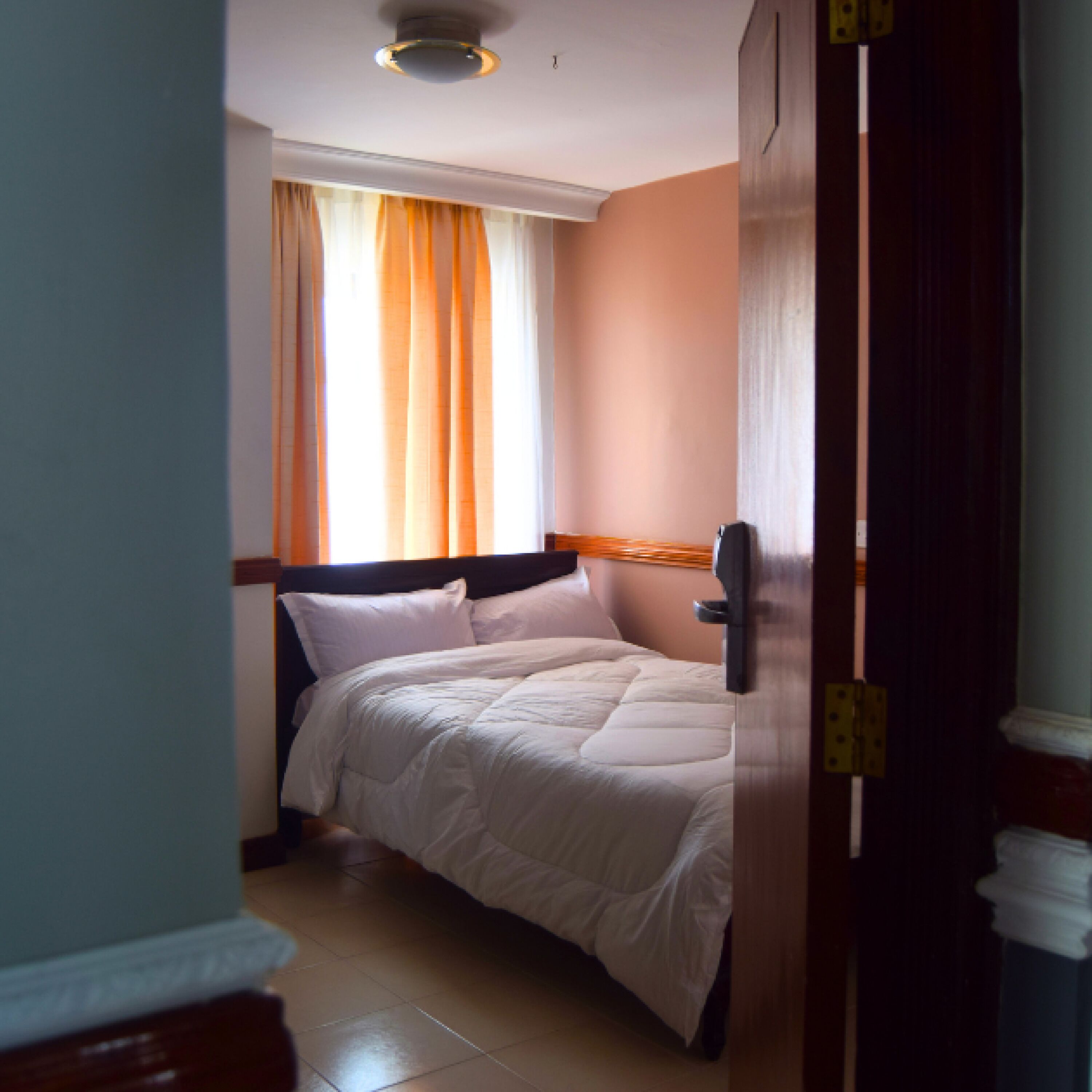 A hotel room with a bed, a window with curtains, and a door.