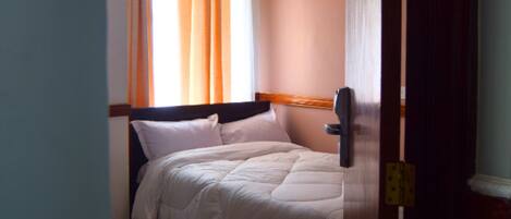 A hotel room with a bed, a window with curtains, and a door.