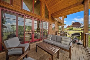 Una terraza techada con mobiliario de madera, grandes puertas correderas de vidrio y vistas del paisaje circundante.