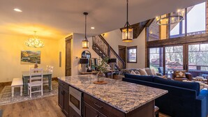 A spacious living area with a large island, a blue sofa, and a staircase leading to an upper level. - Timberline at Eagles Nest - Village with Views! (Banner Elk)