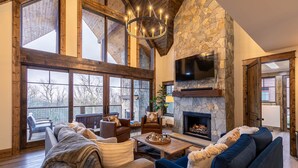 A spacious living room with a stone fireplace, large windows, and a cozy seating area. - Timberline at Eagles Nest - Village with Views! (Banner Elk)