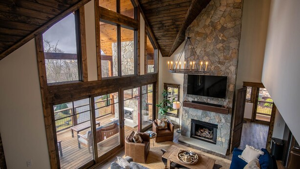 A spacious living area with a stone fireplace, large windows, and a wooden ceiling. - Timberline at Eagles Nest - Village with Views! (Banner Elk)