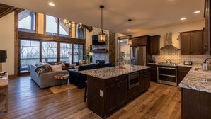 A spacious kitchen with dark wood cabinets, granite countertops, and stainless steel appliances. There is a large island with a built-in oven and a seating area with a sofa and chairs. - Timberline at Eagles Nest - Village with Views! (Banner Elk)
