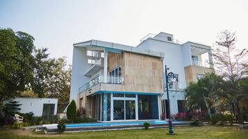 Stylish two-story building with a flat roof and balcony, surrounded by lush gardens and a small pool.