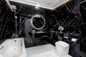 Ein modernes Badezimmer mit schwarzem Marmordesign, einer großzügigen Badewanne, einem runden Spiegel und einer Toilette.