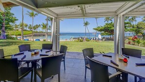 An outdoor dining area with tables and chairs, overlooking a beach and ocean.