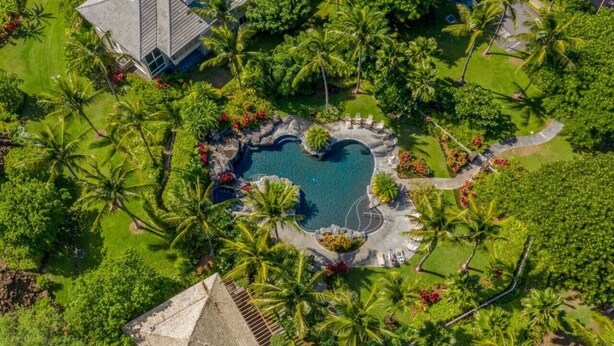 An aerial view of a resort with a central swimming pool surrounded by palm trees and a small waterfall.