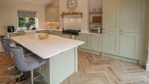 Una cocina con una isla central, taburetes de bar, estufa, un reloj y armarios de madera.