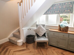 A staircase leading to a landing with a grey chair and a small table with a vase. - Netherdale House (Buxton)