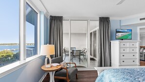 Ein Hotelzimmer mit Balkon, einem Bett, einem Schreibtisch mit Lampe, einem Fernseher und Blick aufs Meer.