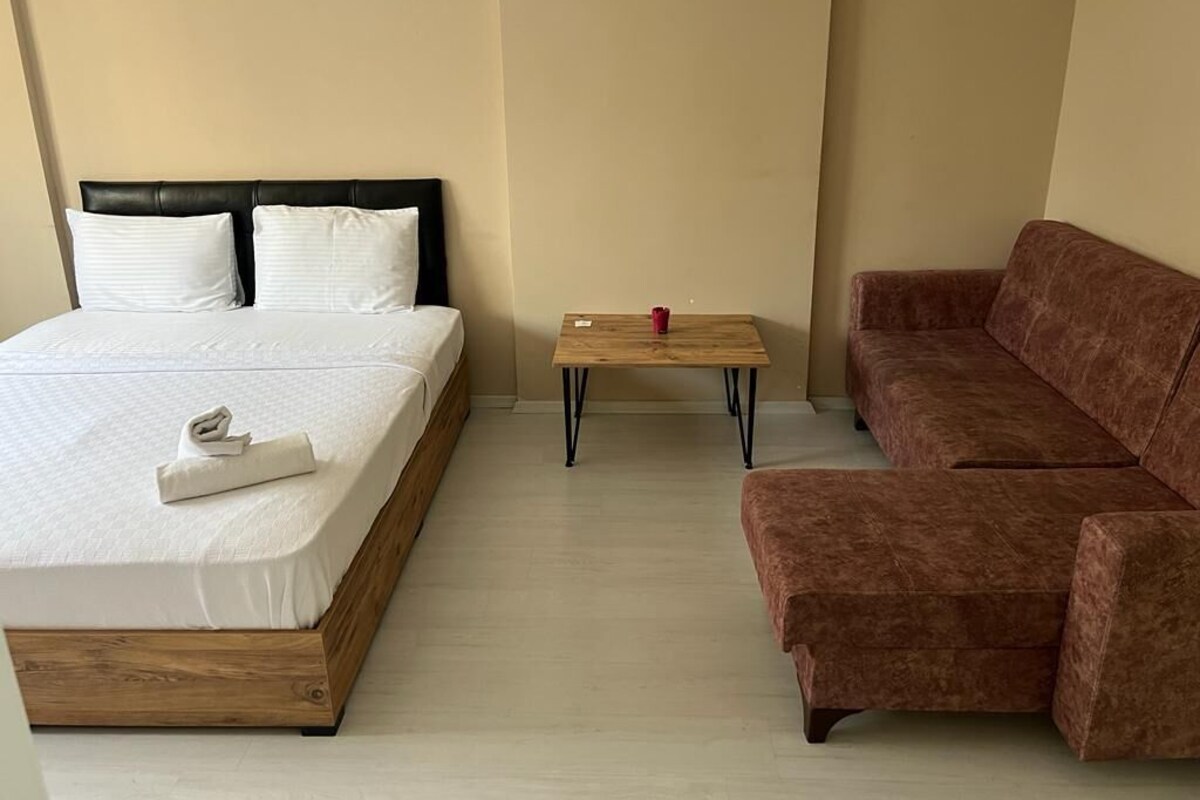 A room with a bed, a wooden nightstand, a brown sofa, and a small table.