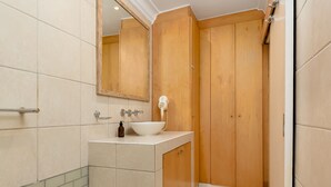 Un bagno con lavandino bianco, mobili in legno, uno specchio e una zona doccia.