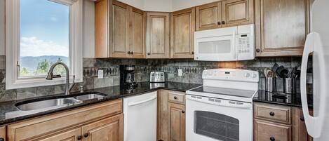 Una cocina con armarios de madera, un lavamanos de acero inoxidable, una estufa blanca y un microondas.