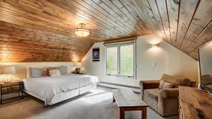 A cozy attic bedroom with a wooden ceiling, a large bed, a sofa, and a small table. - 1107 American Way (Breckenridge)