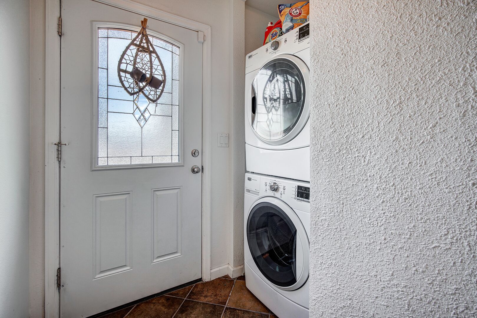 Un lavadero con una puerta blanca, un ventanal con detalle metálico decorativo y dos lavadoras de carga frontal apiladas.