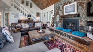 A spacious living room with a stone fireplace, leather sofas, and a high wooden ceiling. - 1107 American Way (Breckenridge)