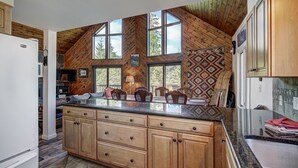 A spacious kitchen with a large island, wooden cabinetry, and large windows offering views of the outdoors. - 1107 American Way (Breckenridge)