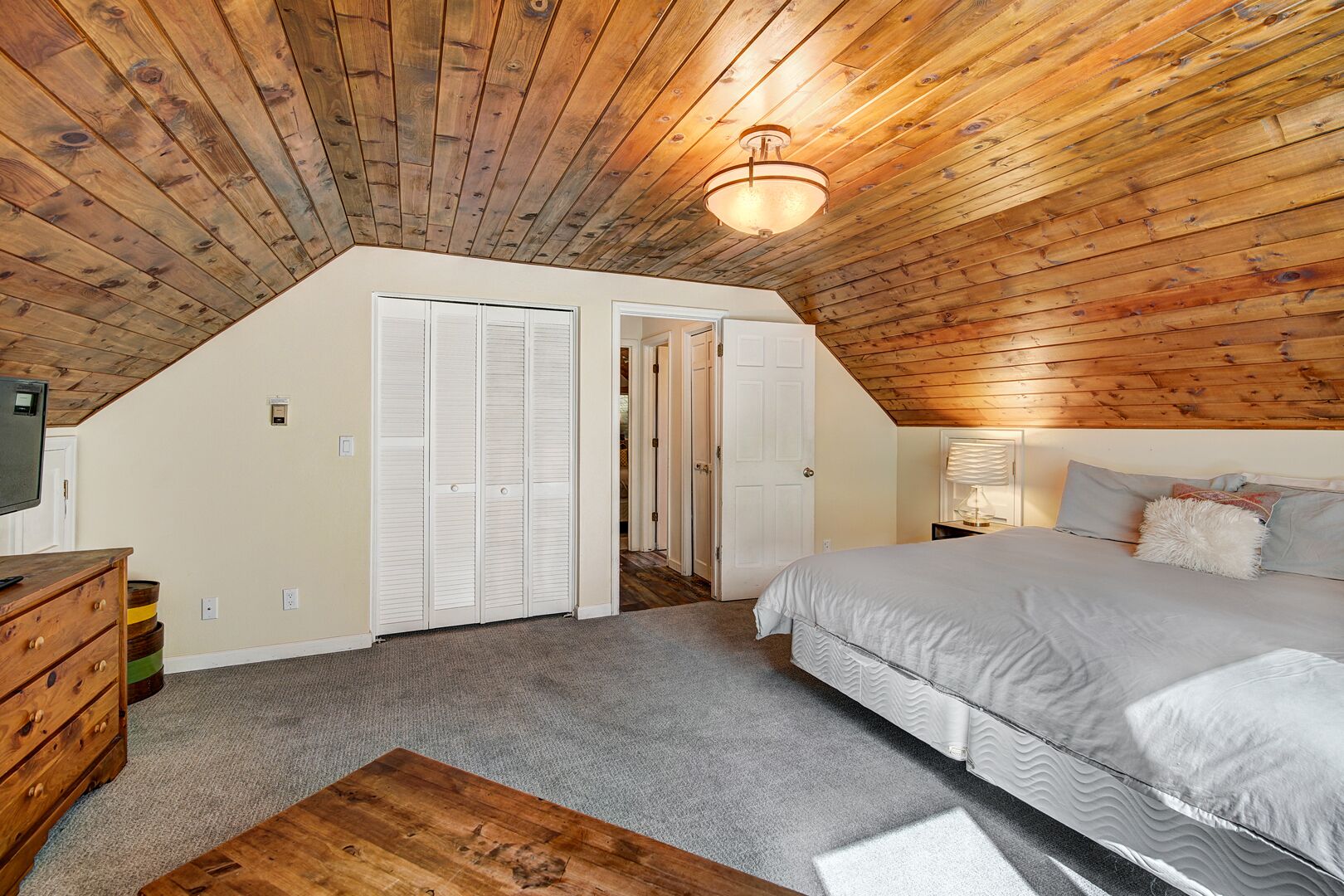 A bedroom with a sloped ceiling, wooden walls, a bed, a nightstand, and a dresser.