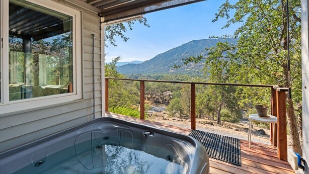 Un bain à remous sur une terrasse en bois, avec vue sur les montagnes et les arbres.