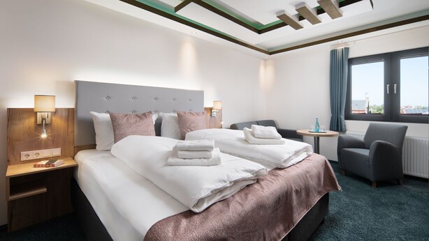 A hotel room with two beds, a desk, a chair, and a window with a view. - Nordseehotel Tausendschön (Wittmund)