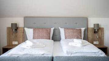 A double bed with white linens and two pillows, a grey headboard, and wooden nightstands with lamps.