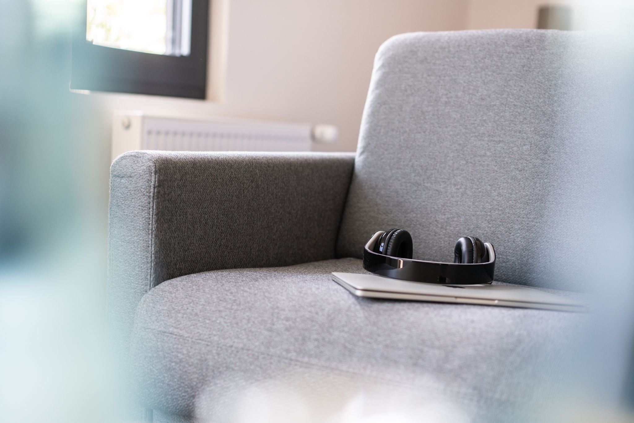A grey sofa with a laptop and black headphones on it.