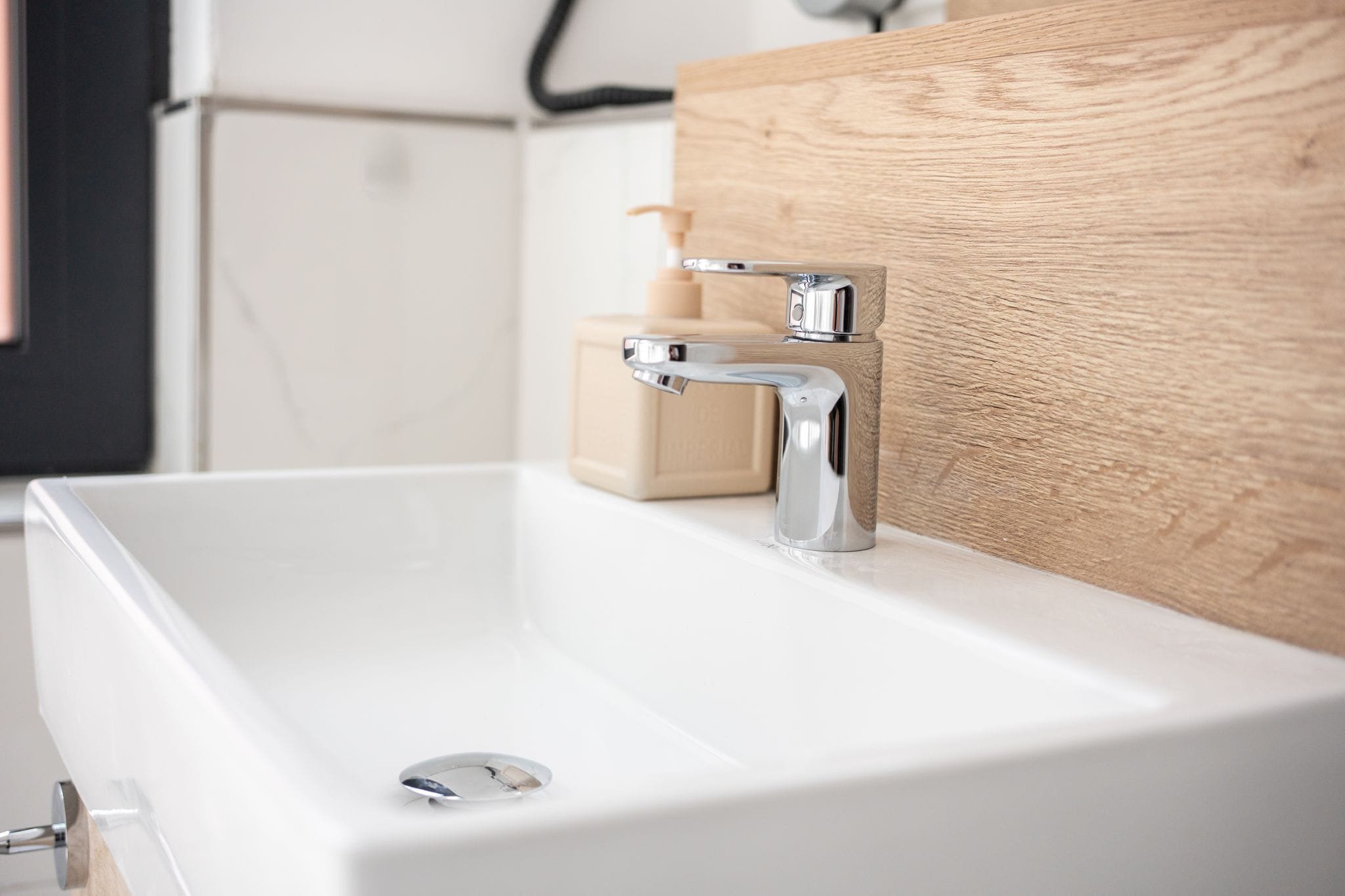 A modern bathroom with a white sink, chrome faucet, and wooden paneling.