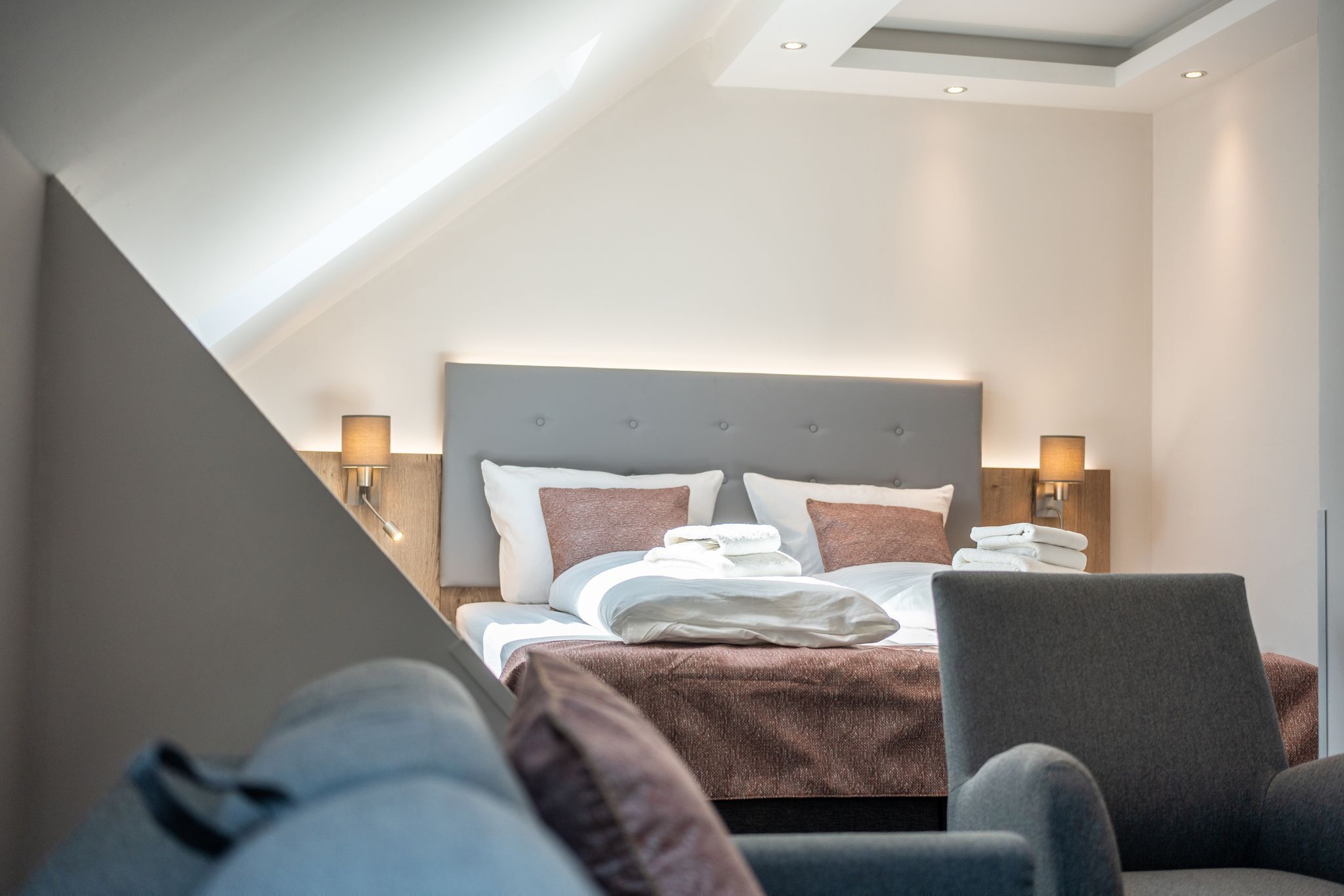 Una habitación de hotel moderna con una cama grande, dos lámparas de noche y vistas al cielo a través de un tragaluz.