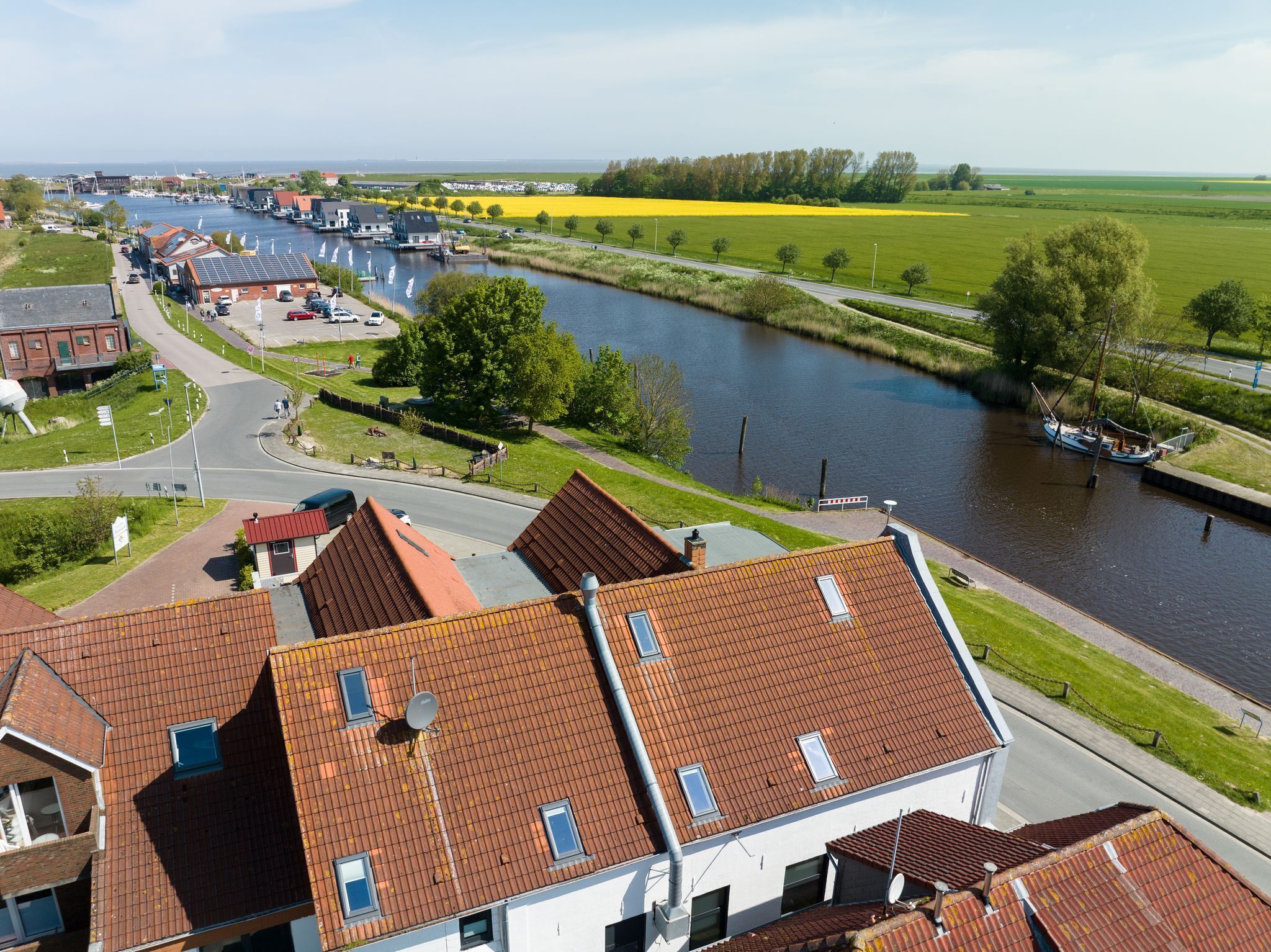 A riverside town with buildings, a canal, and a yellow field in the background.