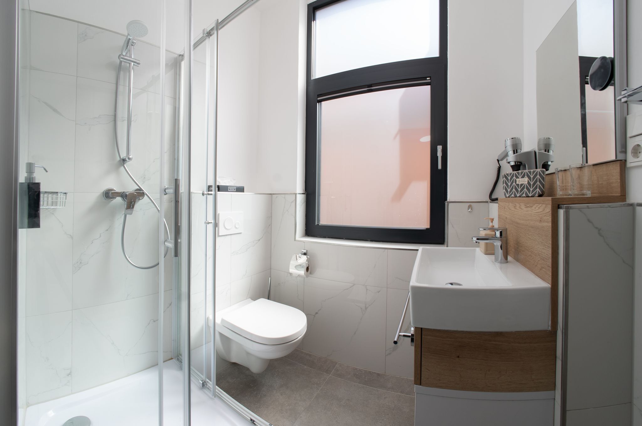 A modern bathroom with a glass-enclosed shower, a white toilet, and a sink with a wooden countertop.