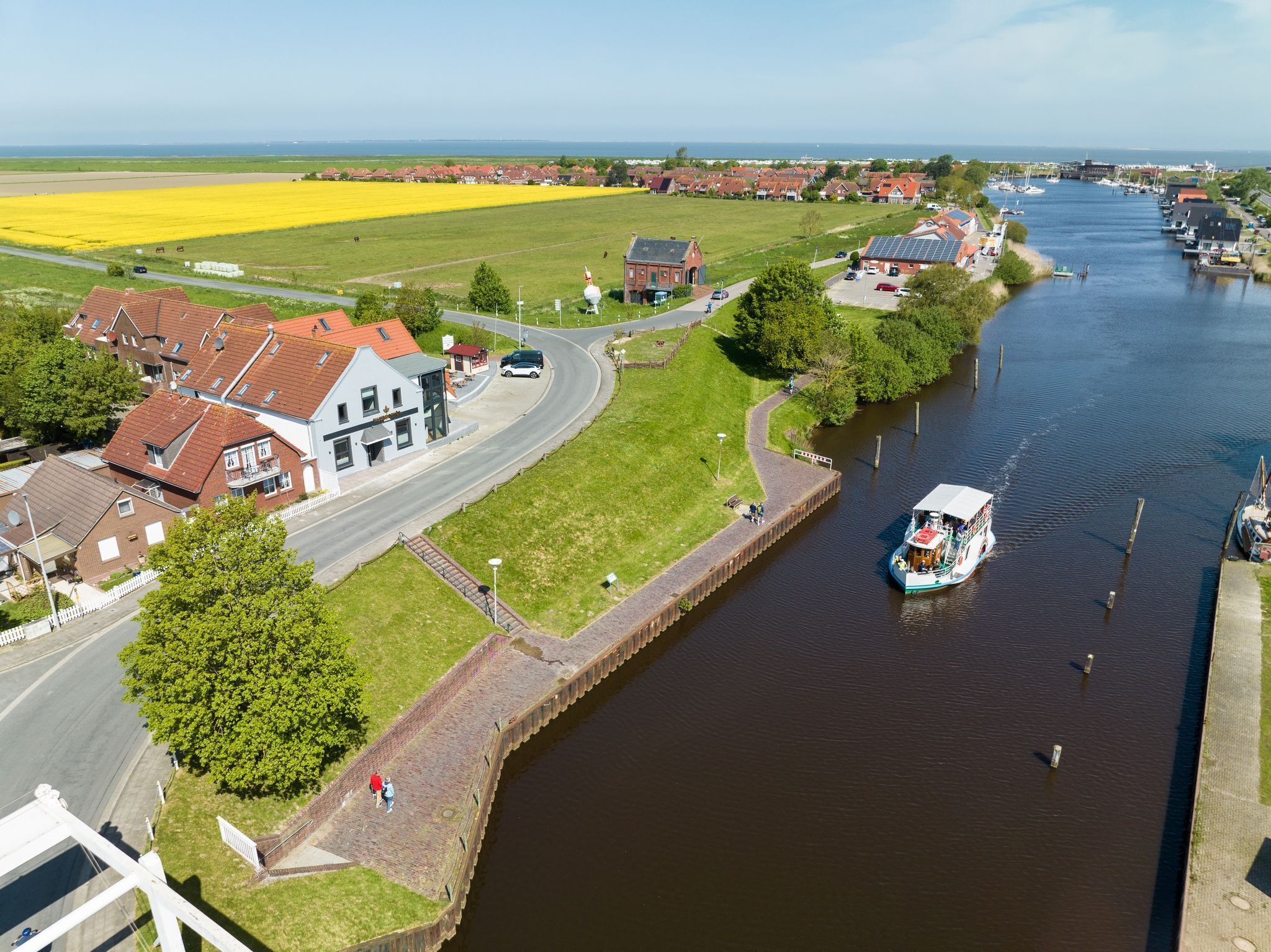 A canal with a boat, houses, and a field of yellow flowers.