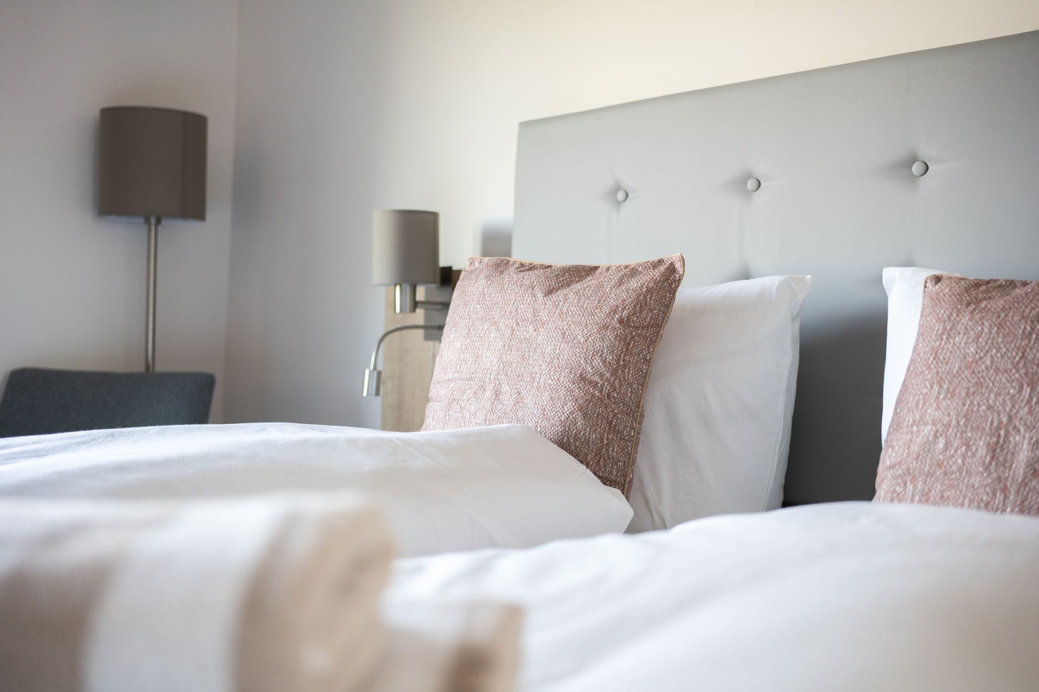 Habitación de hotel con cama, mesita de noche, lámpara y cabecera con botones.