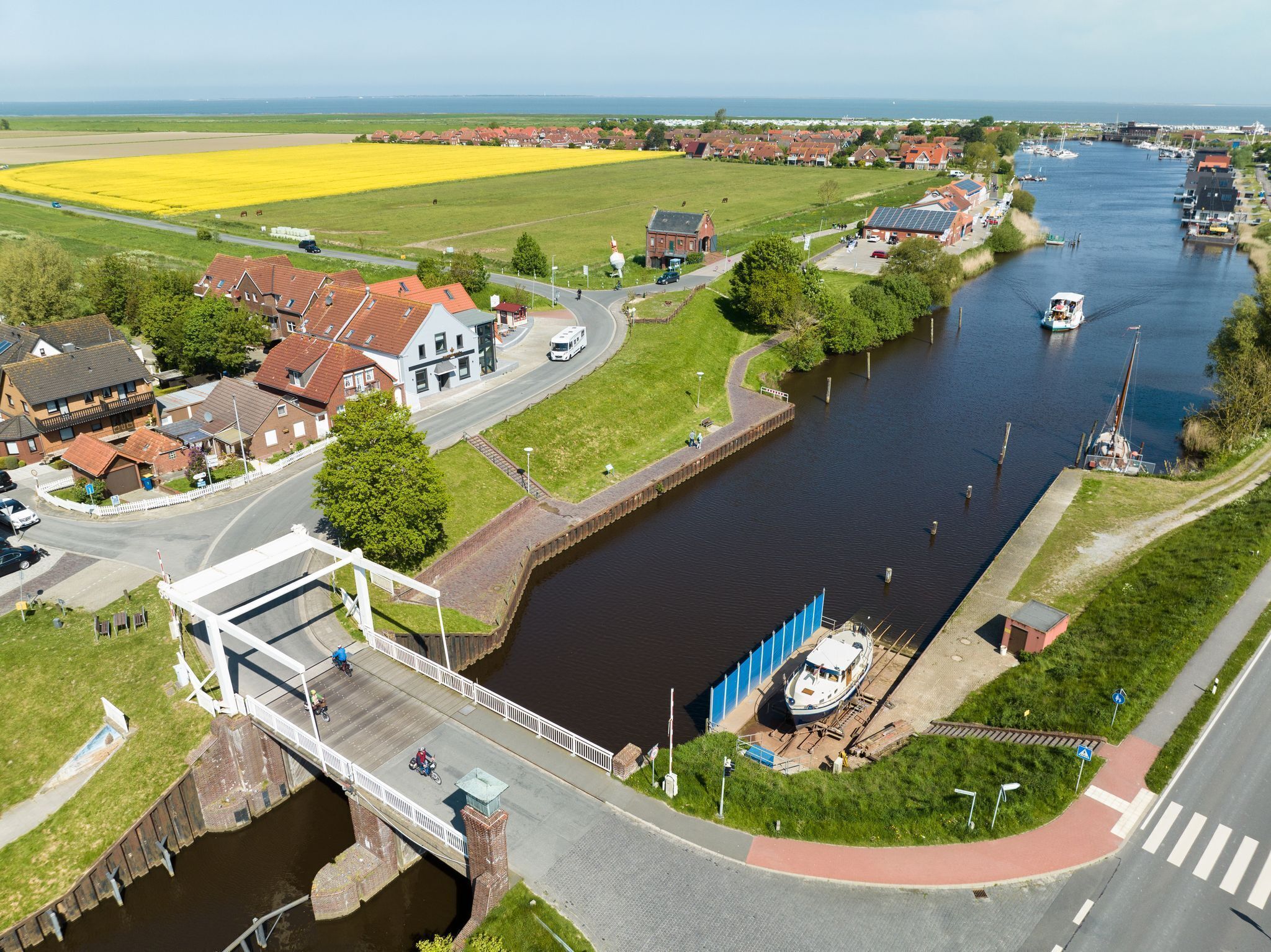 A river with a bridge, a boat dock, and a field of yellow flowers.