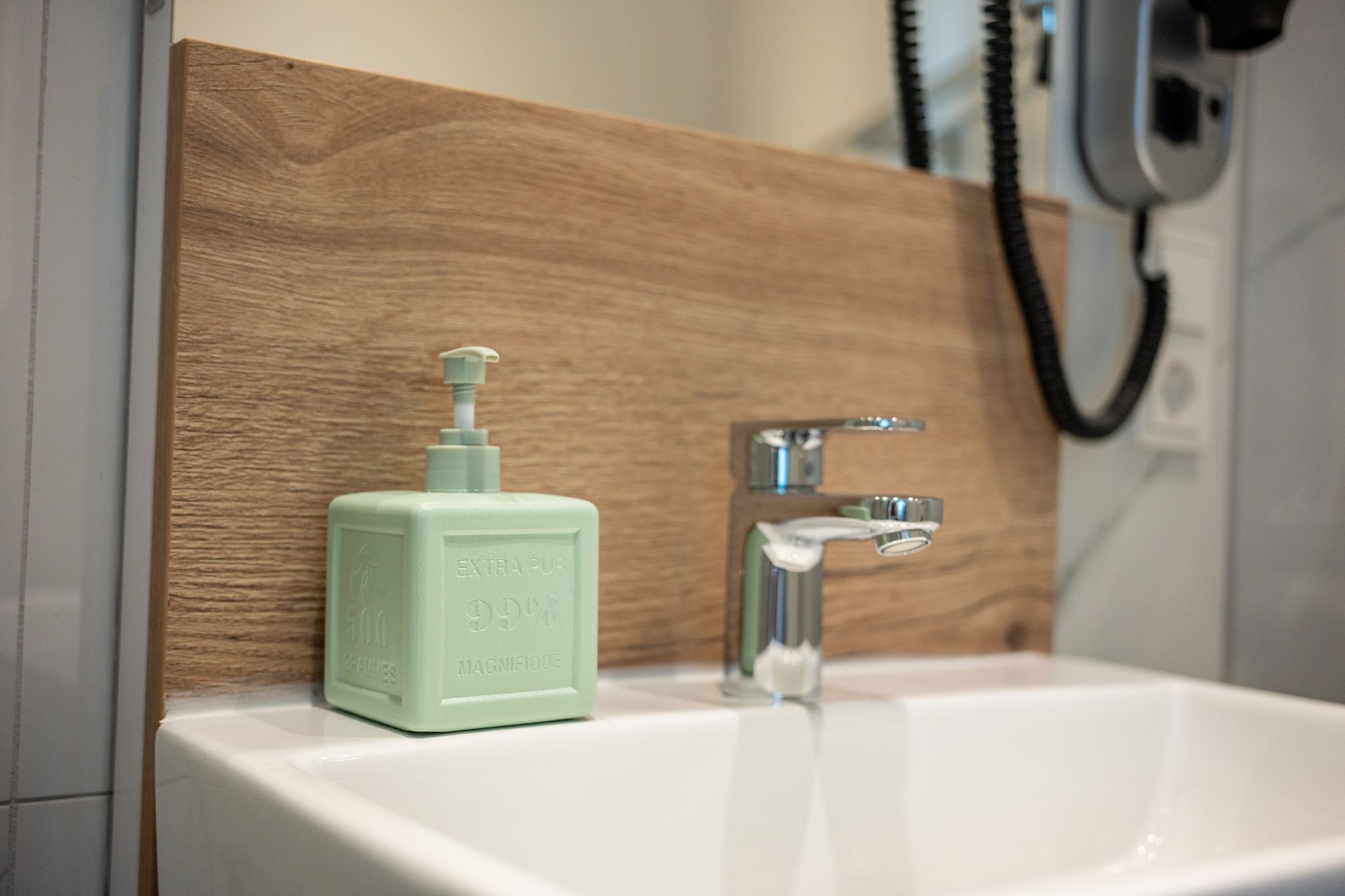 Ein Badezimmer mit einer Holzwandverkleidung, einem weißen Waschbecken und einem grünen Seifenspender.
