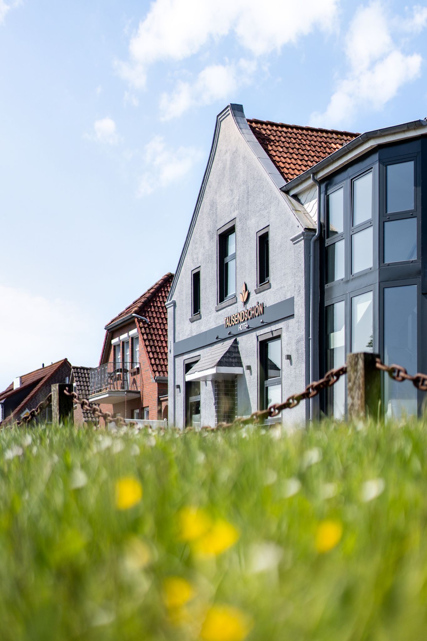 Un hôtel à la façade moderne, avec une enseigne bien visible indiquant « TAUSEND SCHÖN », et une clôture en treillis métallique au premier plan.