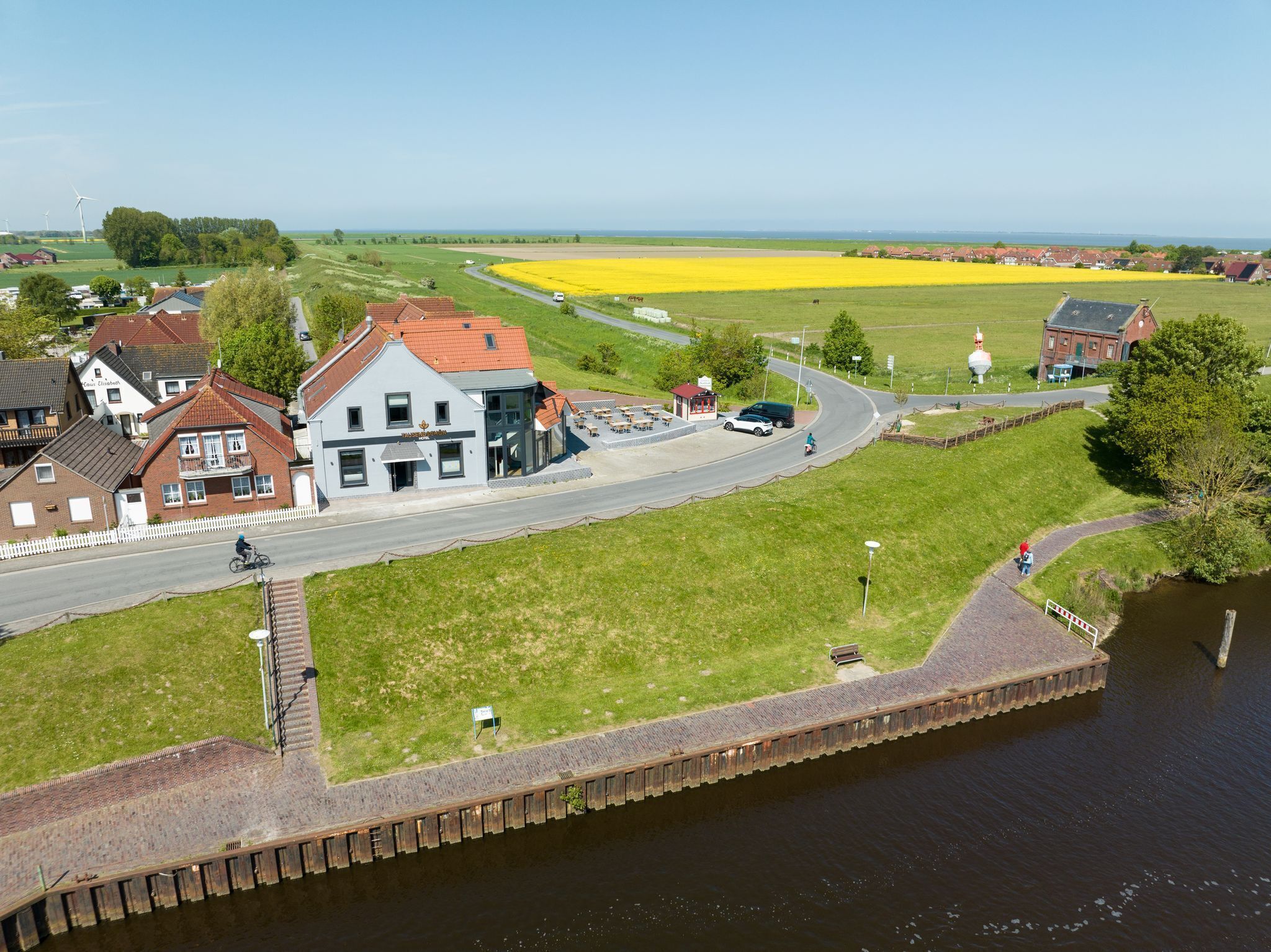 A riverside hotel with a red-roofed building, a grassy area, and a yellow field in the background.