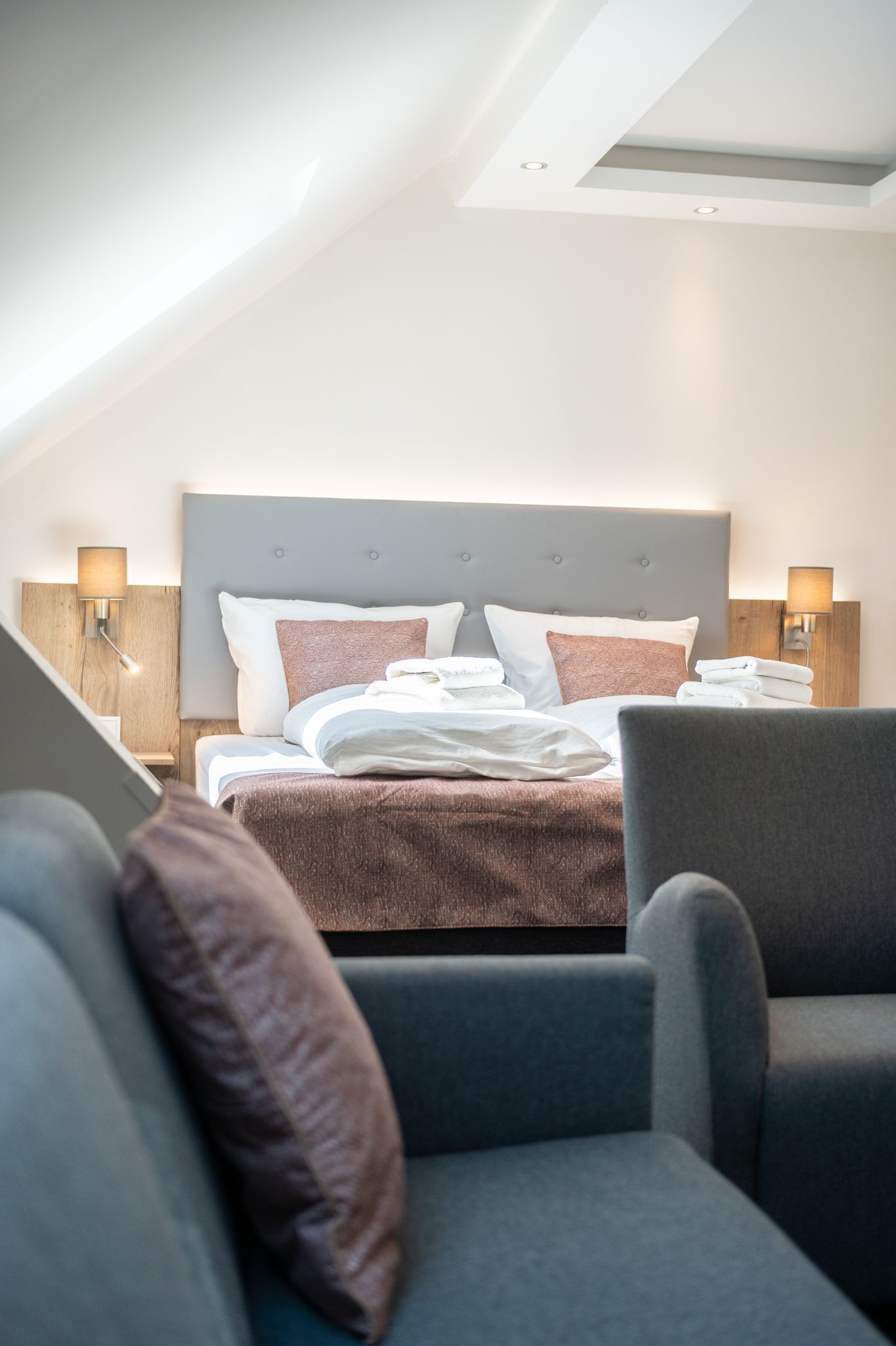 A modern hotel room with a neatly made bed, two bedside lamps, and a sofa.