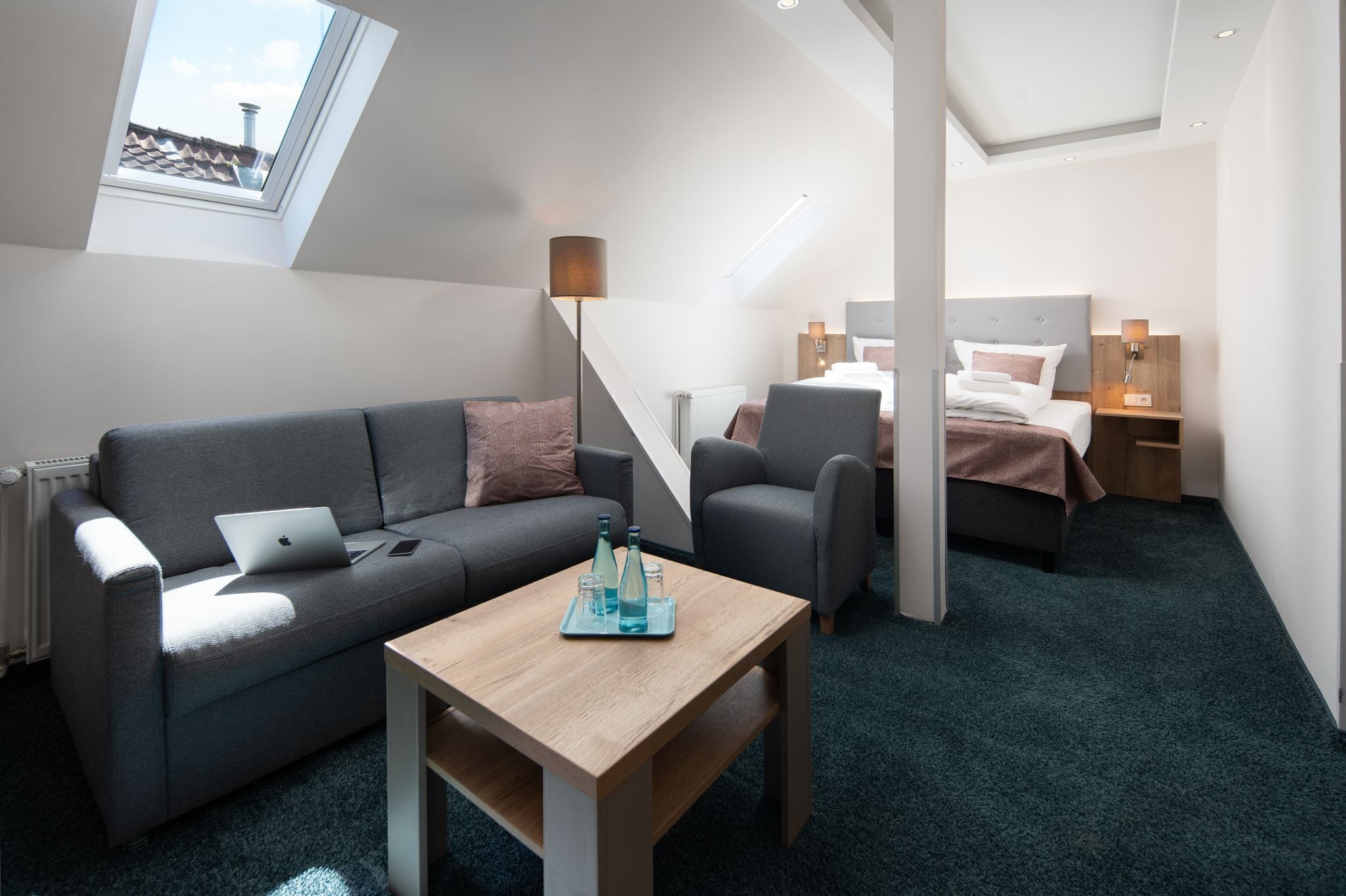 Moderni ja kompakti hotellihuone, jossa on sohva, pieni pöytä, sänky ja kattovalokuvio.