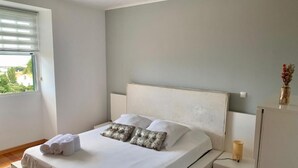 Een slaapkamer met een bed, kussens, een nachtkastje en een raam.