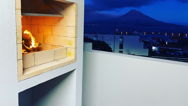 Een balkon met een open haard, uitzicht op een berg en een stadsbeeld in de schemering.