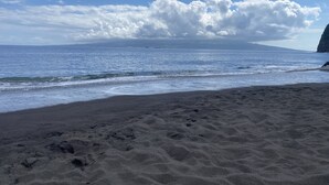 Een strand met donker zand en zachte golven.
