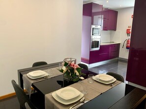Ein Essbereich mit einem Tisch für vier Personen, eine Küche mit violetten Schränken und ein Feuerlöscher an der Wand.