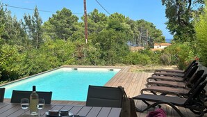 Area piscina con un pontile di legno, sedie a sdraio, un tavolo apparecchiato con una bottiglia di vino, bicchieri e un cappello.